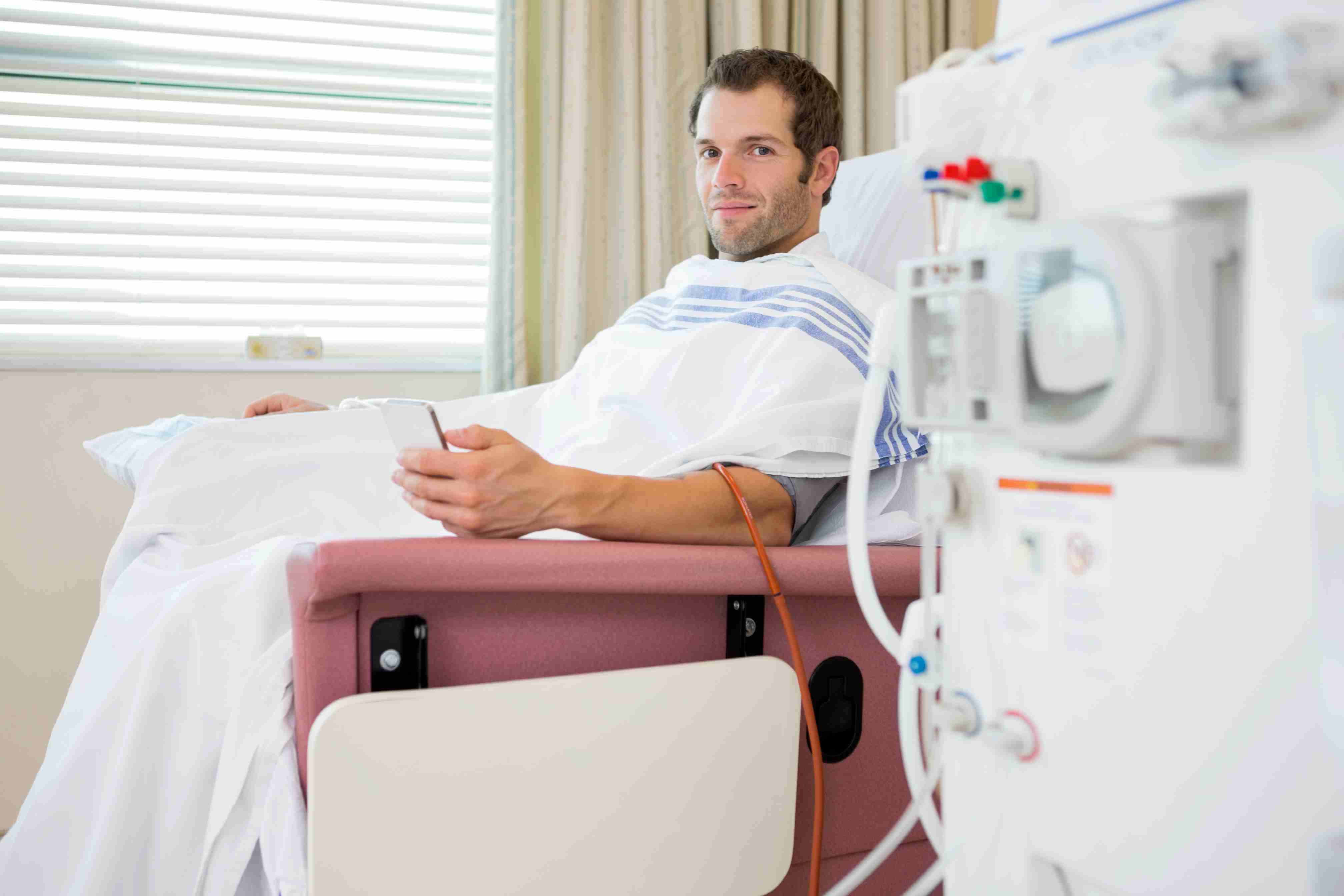 A dialysis patient resting in a treatment chair beside a haemodialysis machine, using a phone